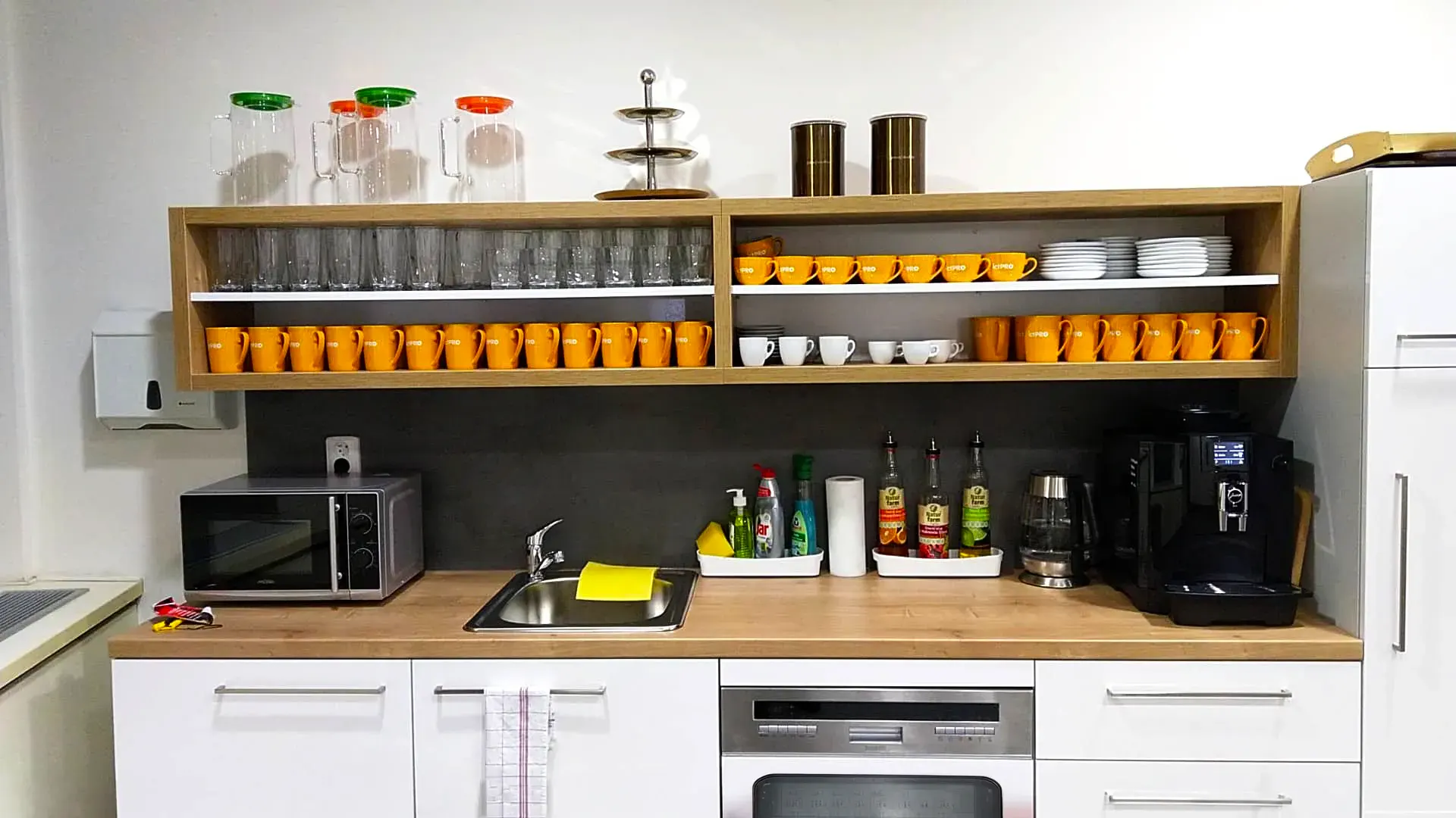 Fully equipped kitchenette with a coffee machine, microwave, sink, and shelves with cups and glasses.
