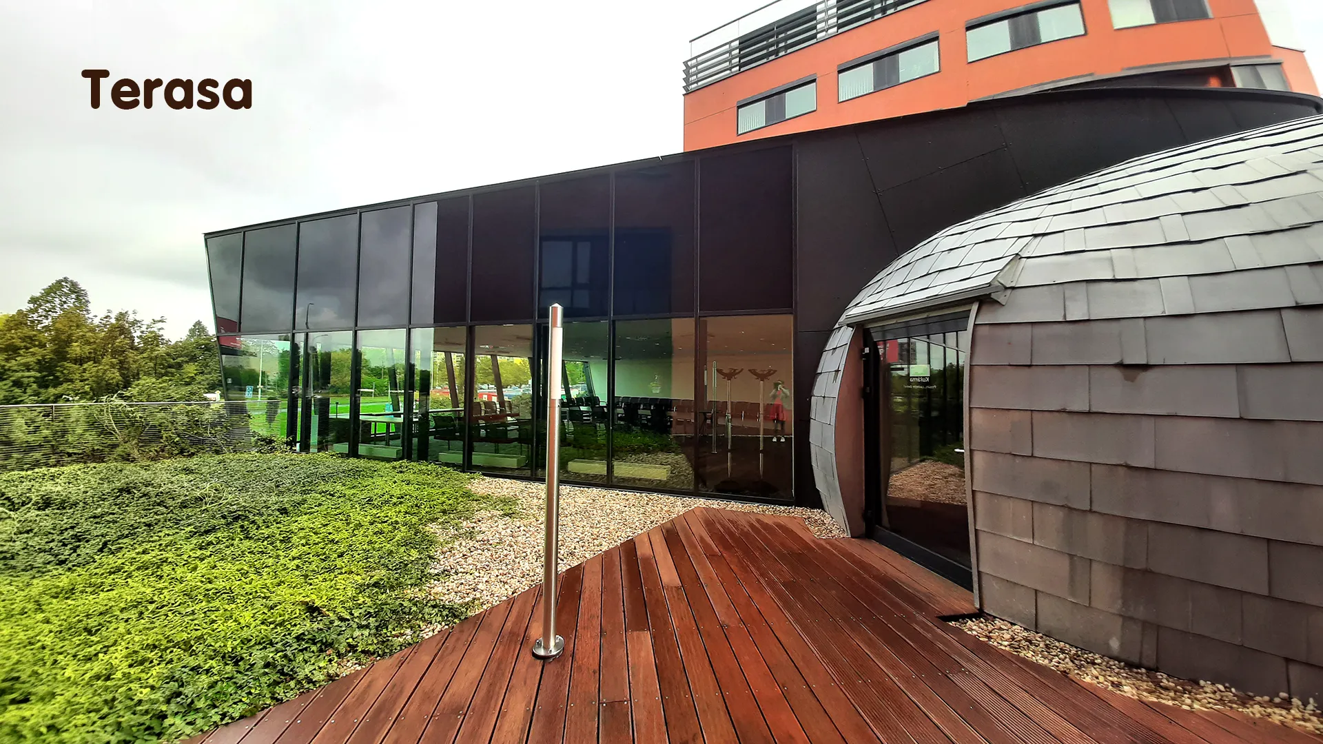 Outdoor wooden terrace with green surroundings by the glass building of the training center.