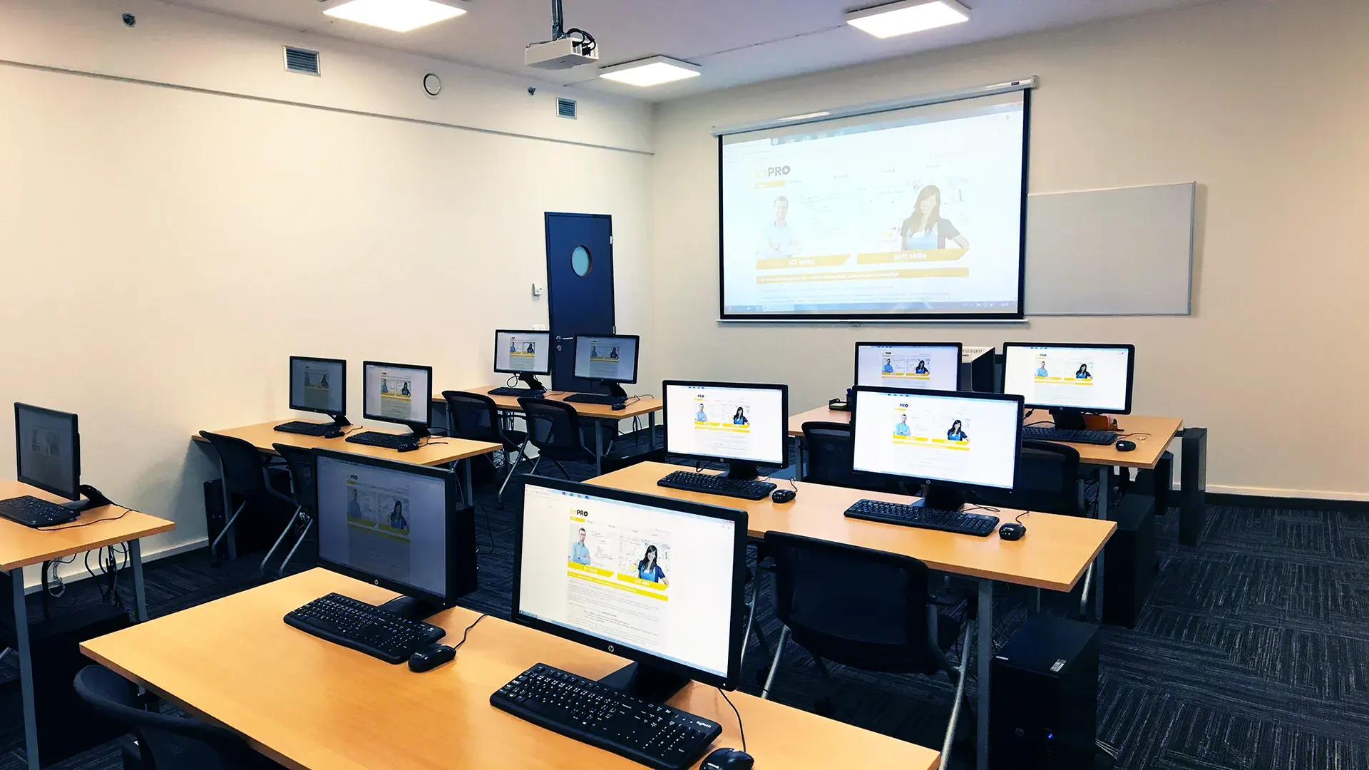 IT classroom with desks, computer monitors, and a projection screen at the front.
